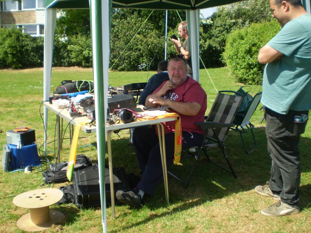 Neil 2E0OYY Rui M7RUI 
Neil operating the radio and talking to Rui M7RUI while behind Niel Kevin 2E0WKV operating the radio and Kevin M7MJW in background checking his phone
